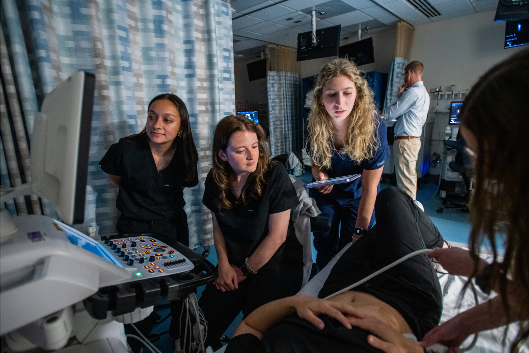 Three students in a simulated hospital suite looking at a mock patient in bed